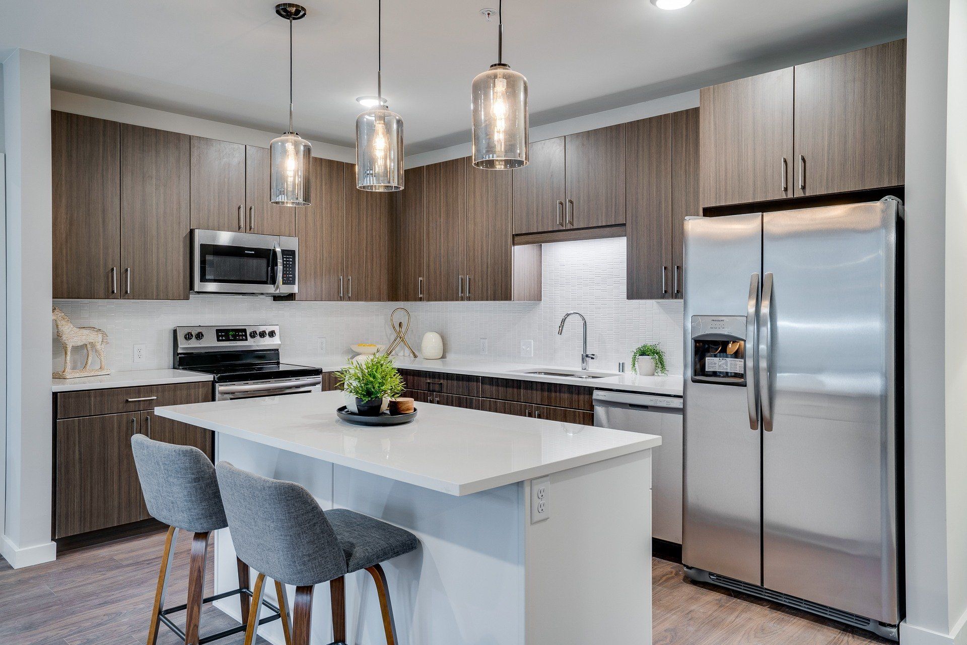 Modern kitchen with dark wood cabinets, stainless steel appliances, and a white island with two gray stools.