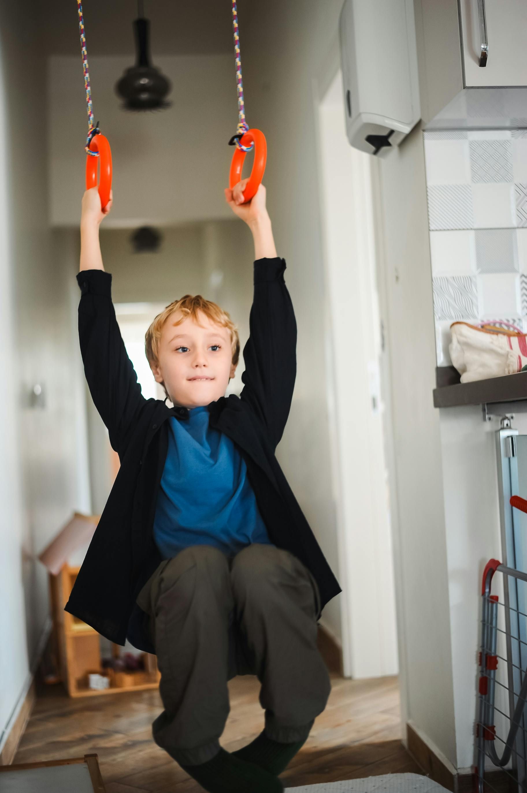 Boy hanging from orange gymnastic rings indoors.