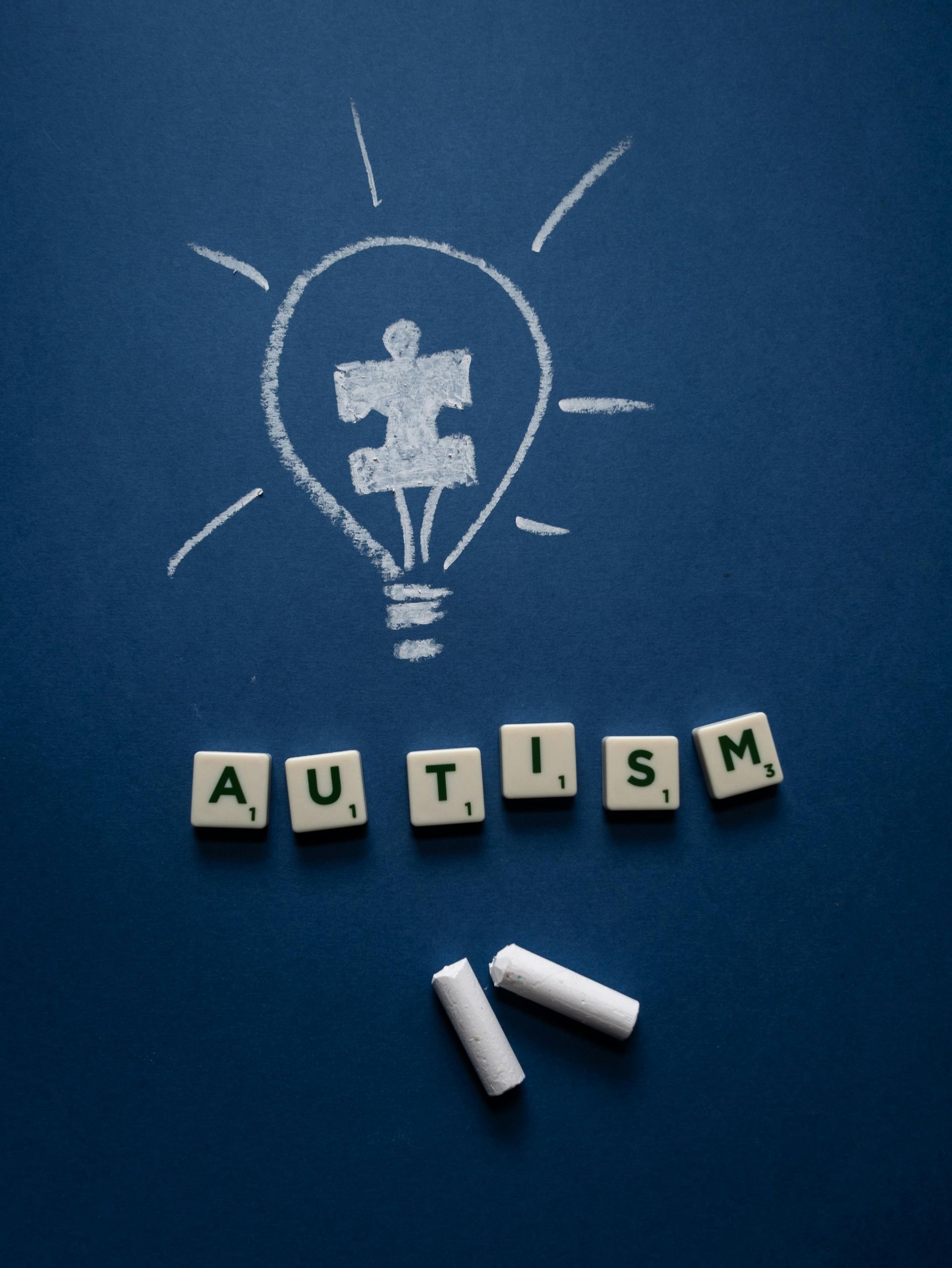 A blue chalkboard with the word "AUTISM" spelled out below a lightbulb with a puzzle piece inside.