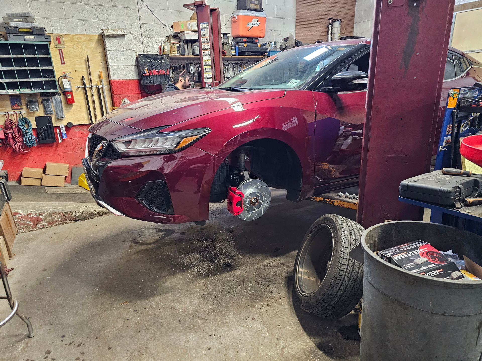 A red car is sitting on a lift in a garage.