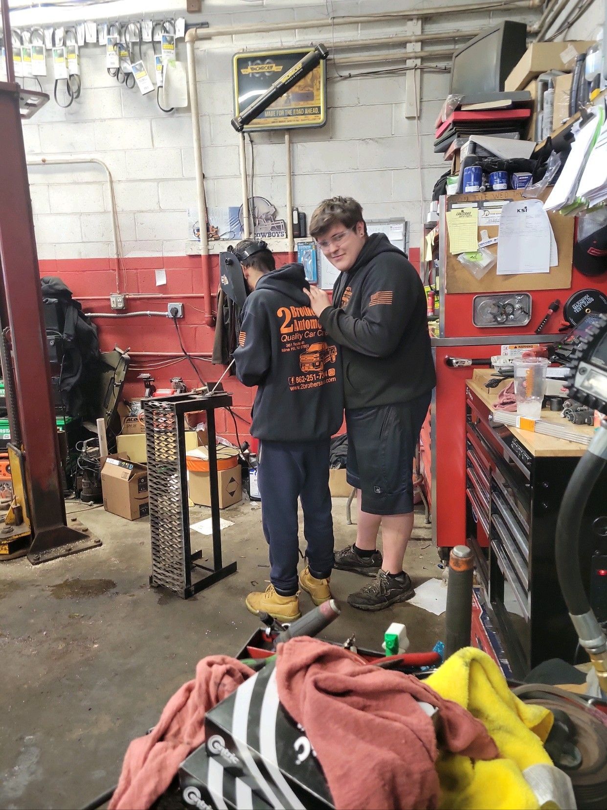 Two men are standing in a garage working on a motorcycle.