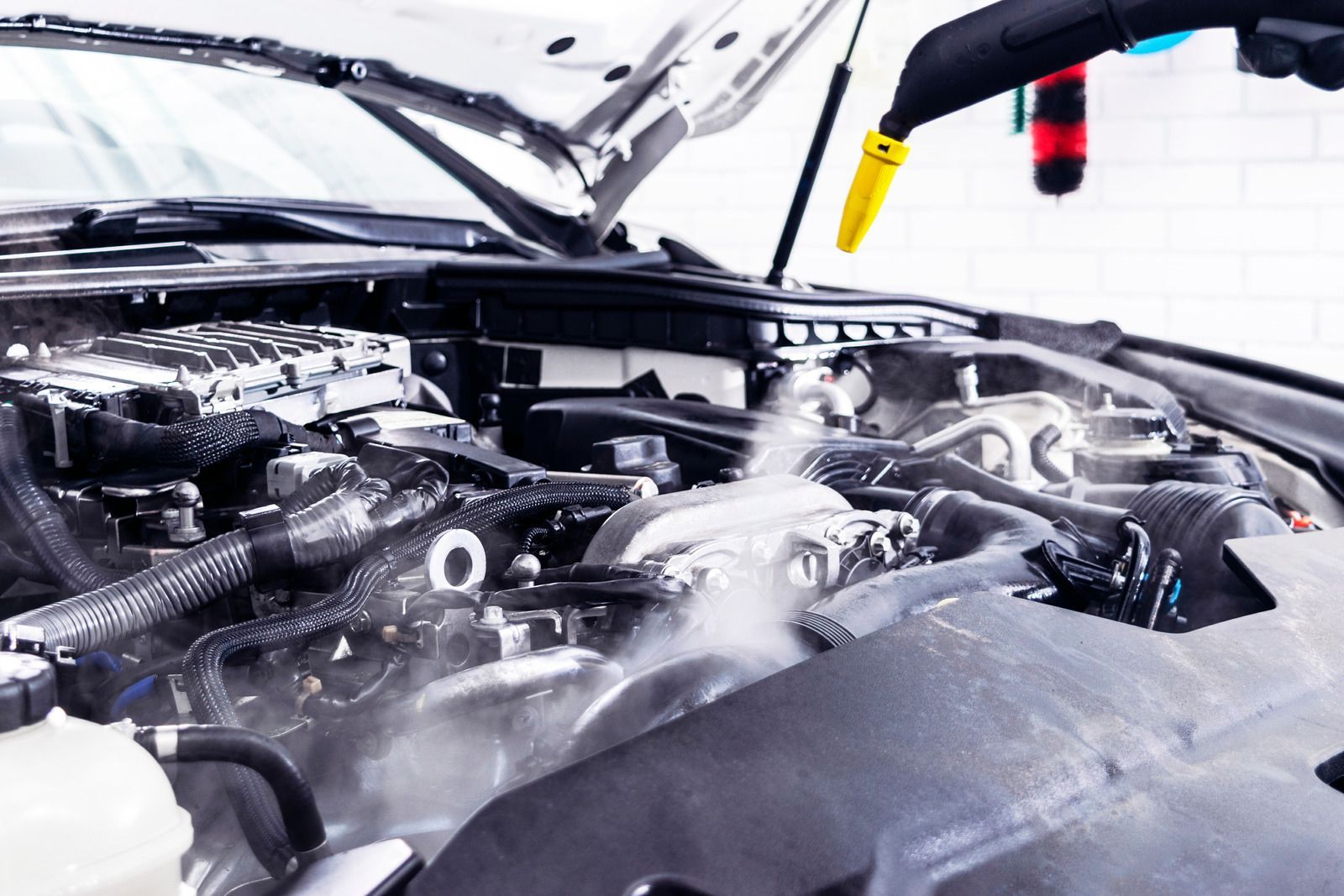 A person is cleaning the engine of a car with a high pressure washer.