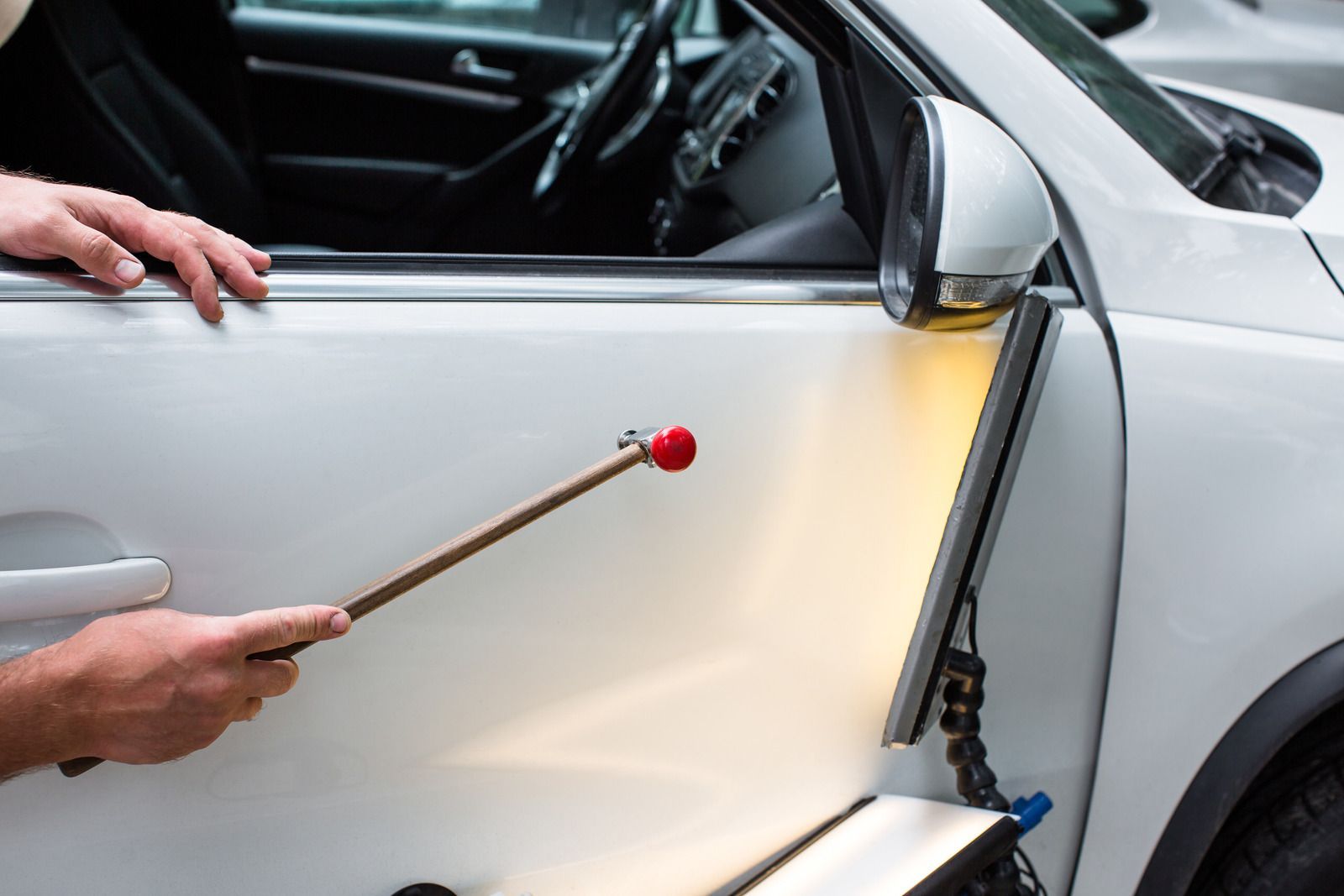 A man is fixing a car door with a hammer.