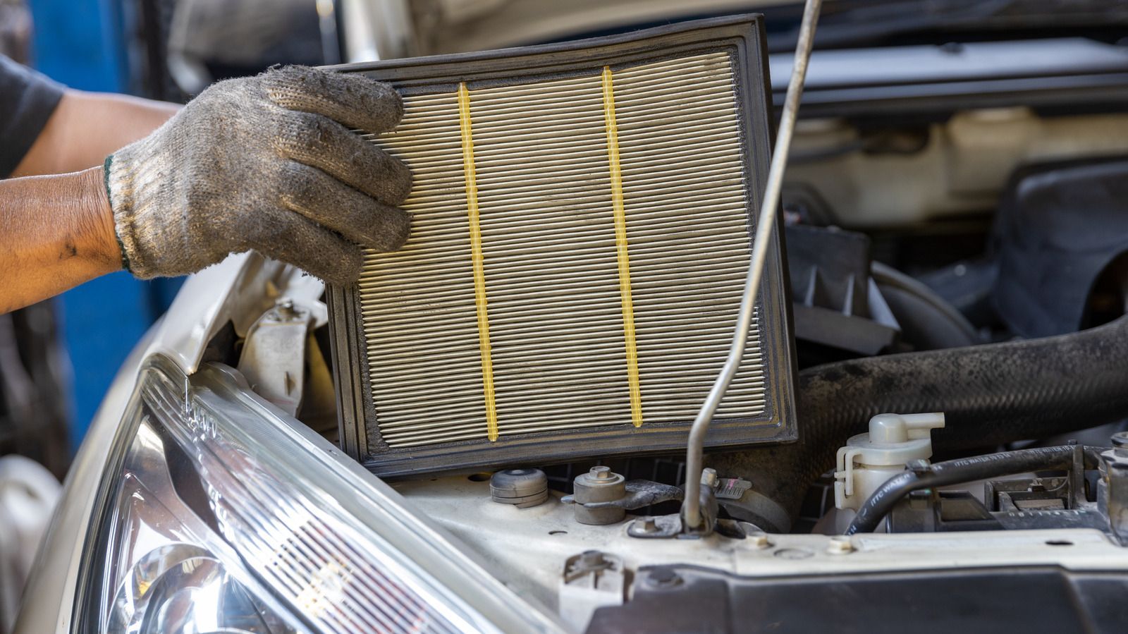 A person is holding a air filter over the hood of a car.