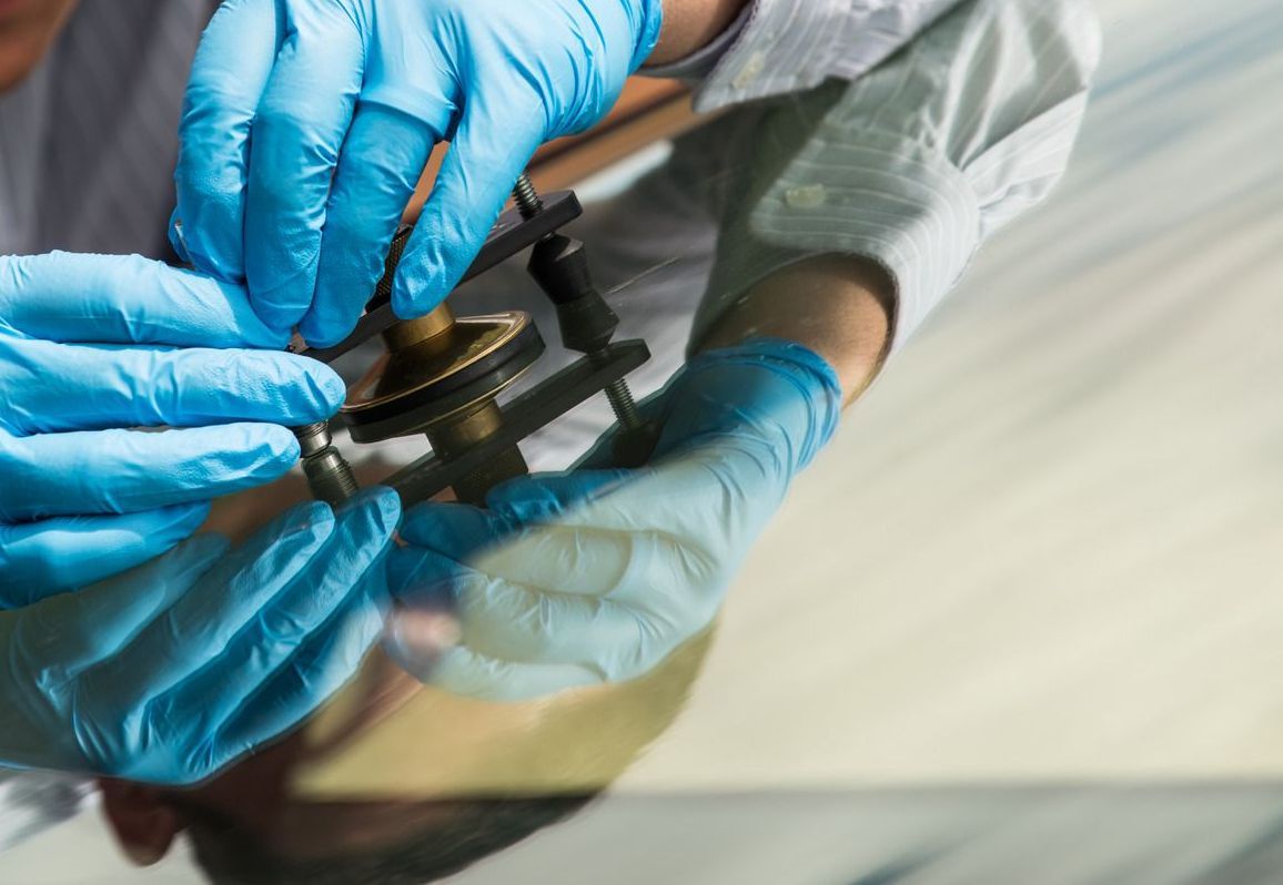 A person wearing blue gloves is working on a car windshield.