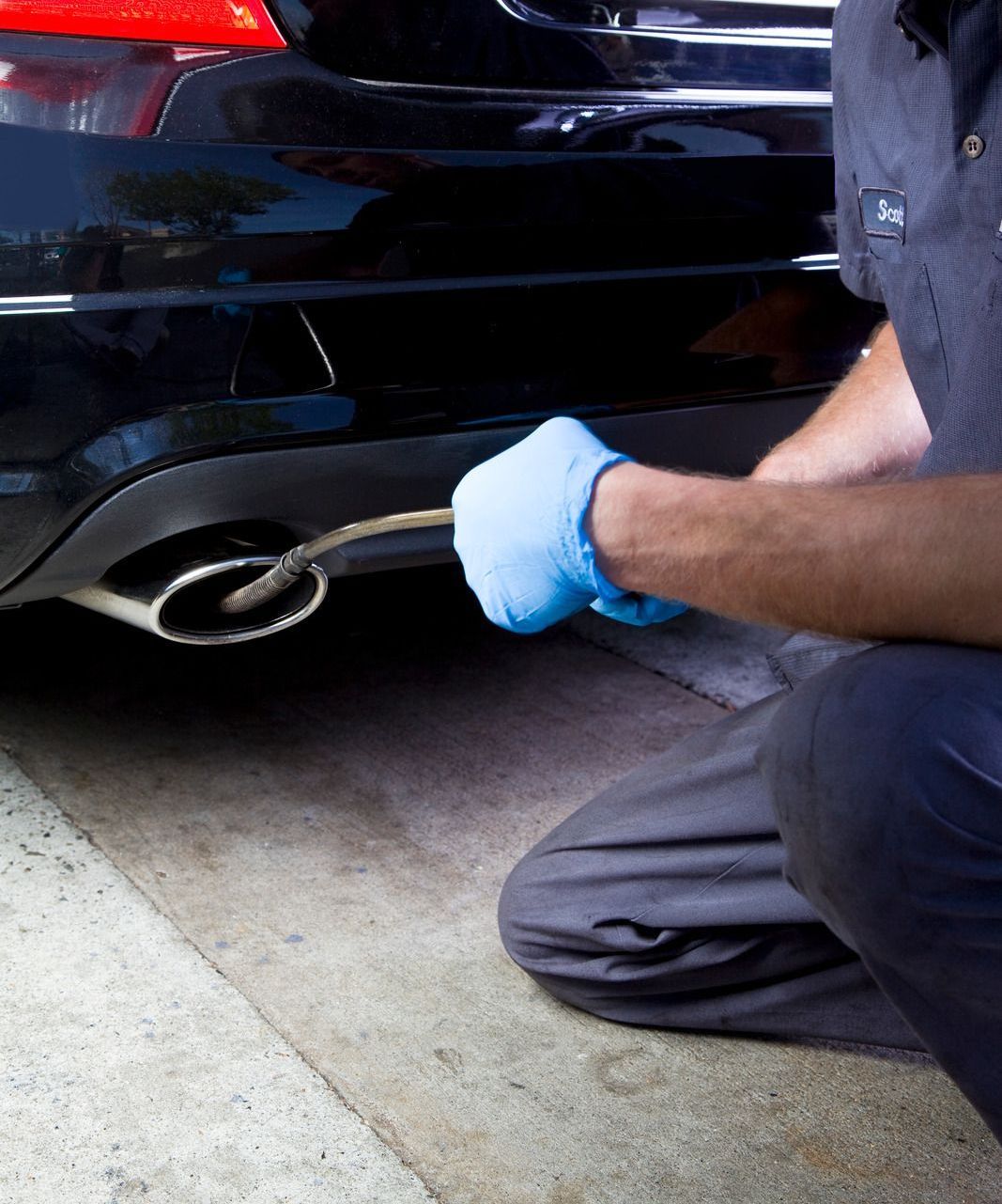 A man wearing blue gloves is working on the exhaust pipe of a car