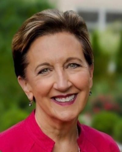 A woman wearing a red jacket and earrings is smiling for the camera.