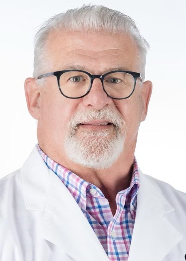 A man with glasses and a beard is wearing a white coat and plaid shirt.