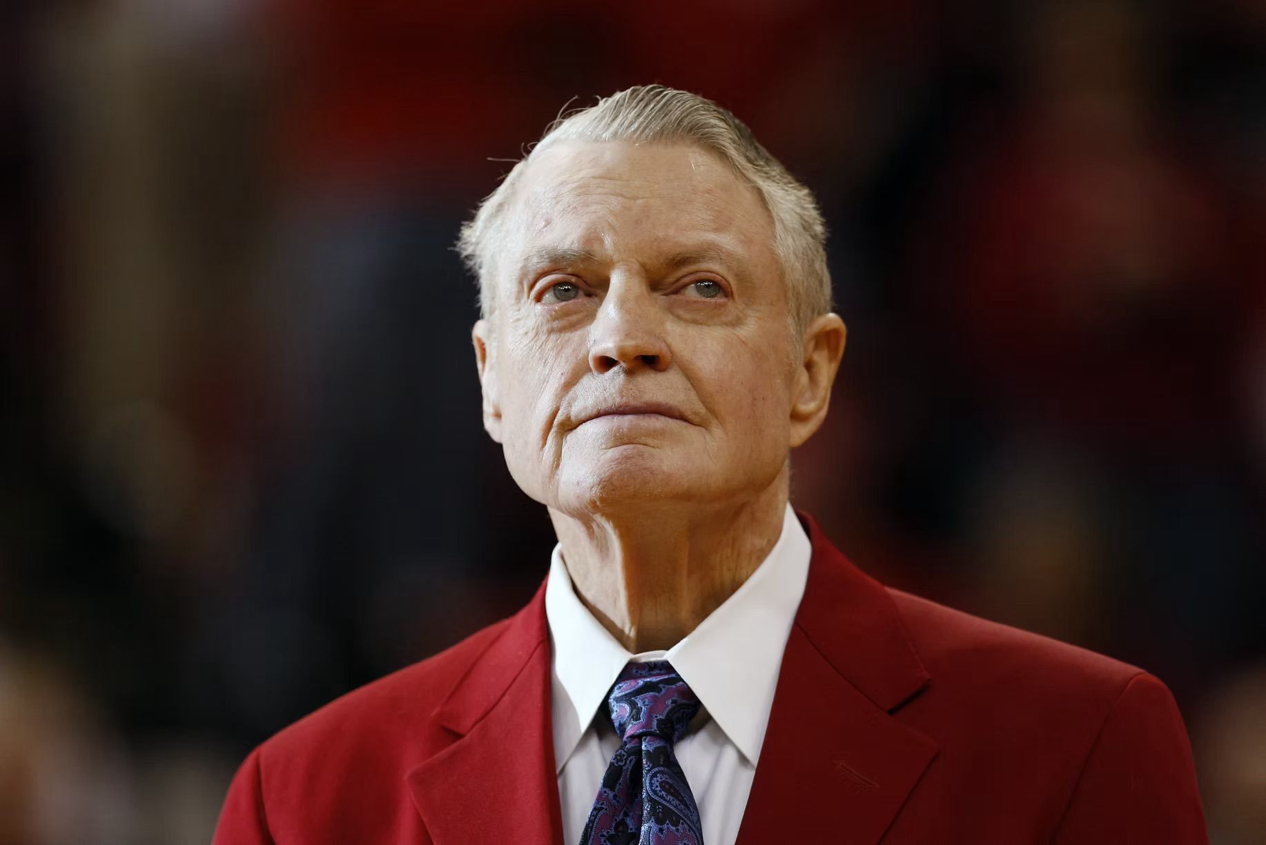 A man in a red suit and tie is standing on a basketball court.