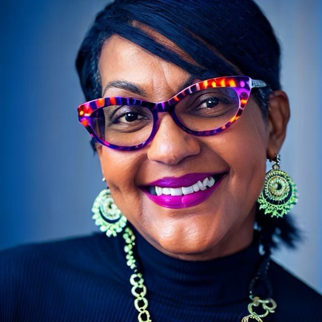 A woman wearing glasses and purple lipstick smiles for the camera