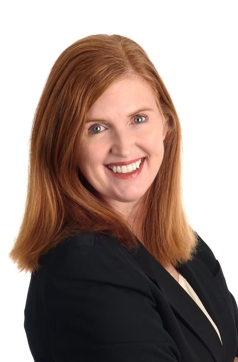 A woman with red hair is wearing a black jacket and smiling.