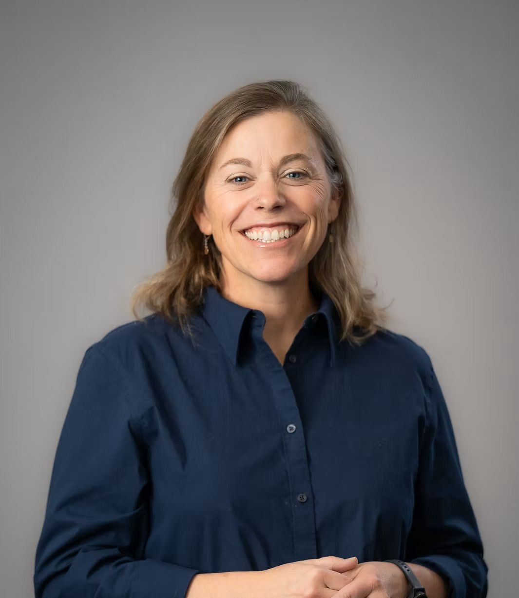 A woman in a blue shirt is smiling for the camera.