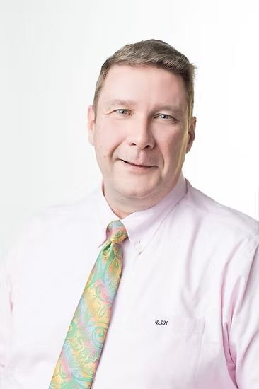 A man in a pink shirt and tie is smiling for the camera.