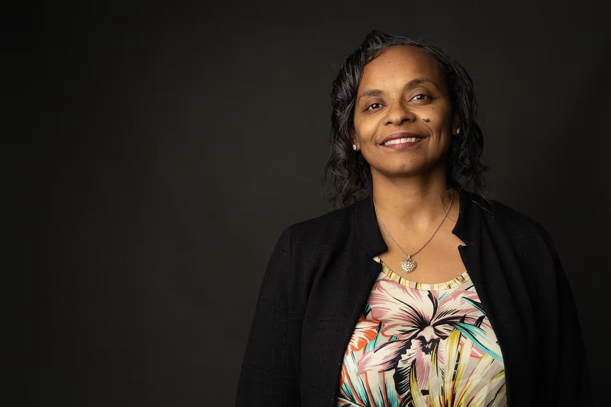 A woman in a black jacket and floral shirt is smiling for the camera.