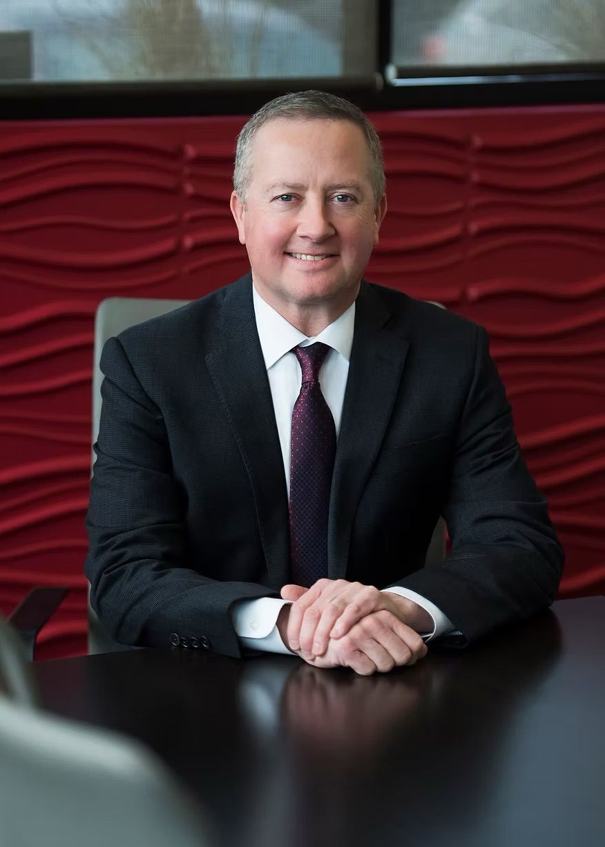 A man in a suit and tie is sitting at a table with his hands folded.