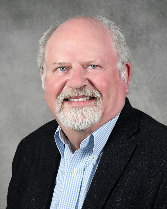 A bald man with a beard is wearing a suit and smiling