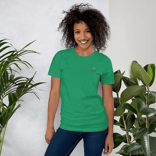 A woman wearing a green t-shirt is standing next to a plant.
