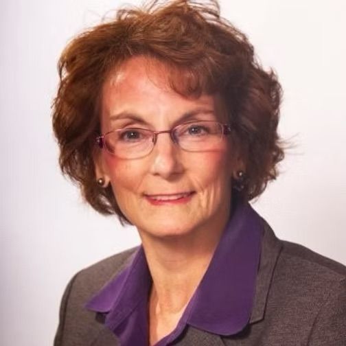 A woman wearing glasses and a purple shirt is smiling for the camera.