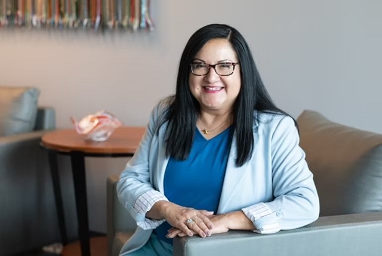 A woman is sitting on a couch wearing glasses and a blue shirt.