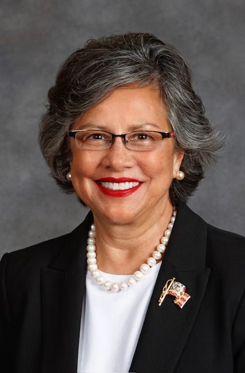 A woman wearing glasses and a pearl necklace smiles for the camera
