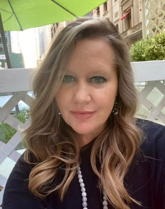 A woman with long hair and a pearl necklace is sitting under a green umbrella.