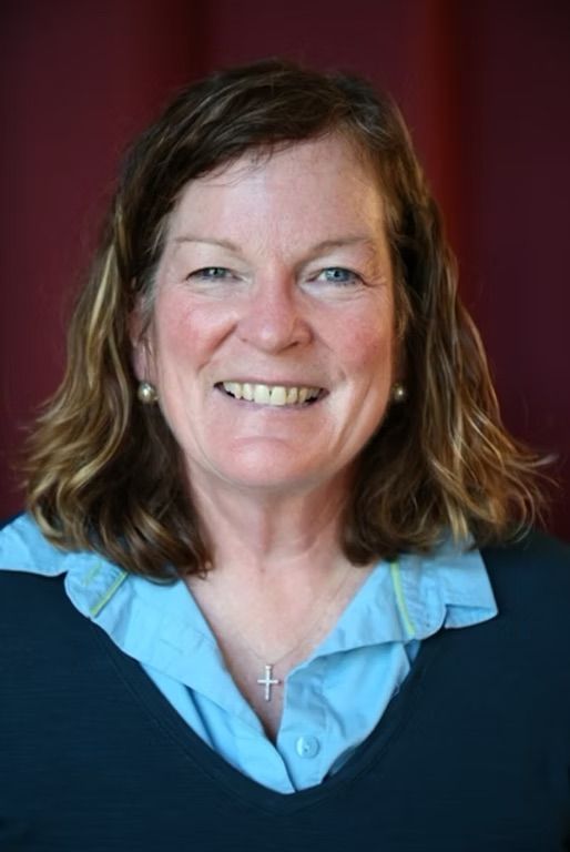 A woman wearing a blue shirt and a black sweater is smiling for the camera.
