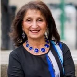 A woman wearing a blue necklace and earrings is smiling for the camera.
