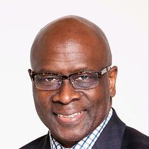 A bald man wearing glasses and a suit is smiling for the camera.