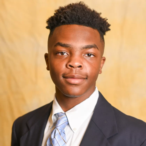 A young man in a suit and tie looks at the camera
