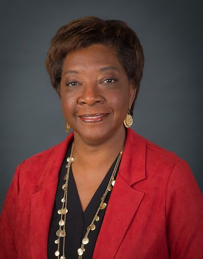 A woman wearing a red jacket and a gold necklace is smiling for the camera.