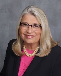 A woman wearing glasses and a pink shirt is smiling for the camera.