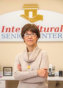 A woman wearing glasses is standing in front of a sign that says inter natural senior center.