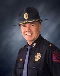A police officer wearing a hat and tie is smiling for the camera.