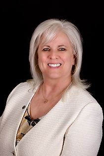 A woman is wearing a white jacket and smiling for the camera.