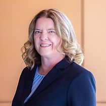 A woman in a suit and blue shirt is smiling for the camera.