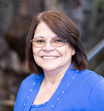 A woman wearing glasses and a blue sweater is smiling for the camera.