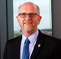 A man in a suit and tie is standing in front of a window.