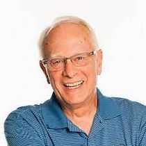 An older man wearing glasses and a blue shirt is smiling.