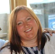 A woman is smiling for the camera while sitting in front of a window.