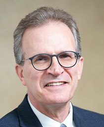 A man in a suit and tie is wearing glasses and smiling.