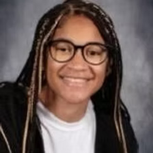 A young woman wearing glasses and braids is smiling for the camera.