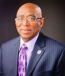 The man is wearing a suit and tie and glasses.