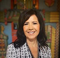 A woman in a black and white jacket is smiling in front of a painting.