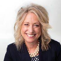 A woman in a blue jacket and pearl necklace is smiling for the camera.