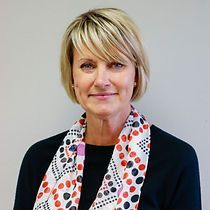 A woman wearing a scarf around her neck is smiling for the camera.
