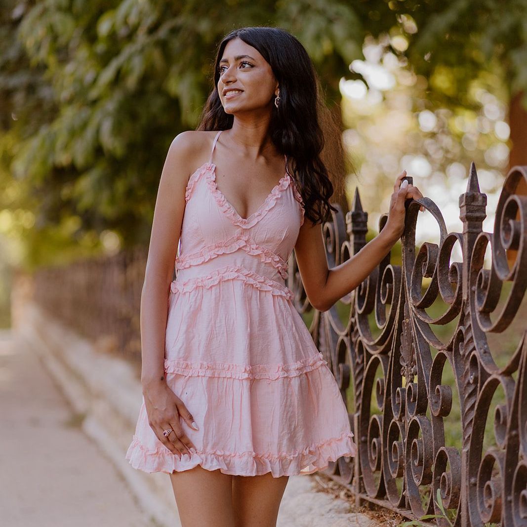 A woman in a pink dress is leaning against a fence.