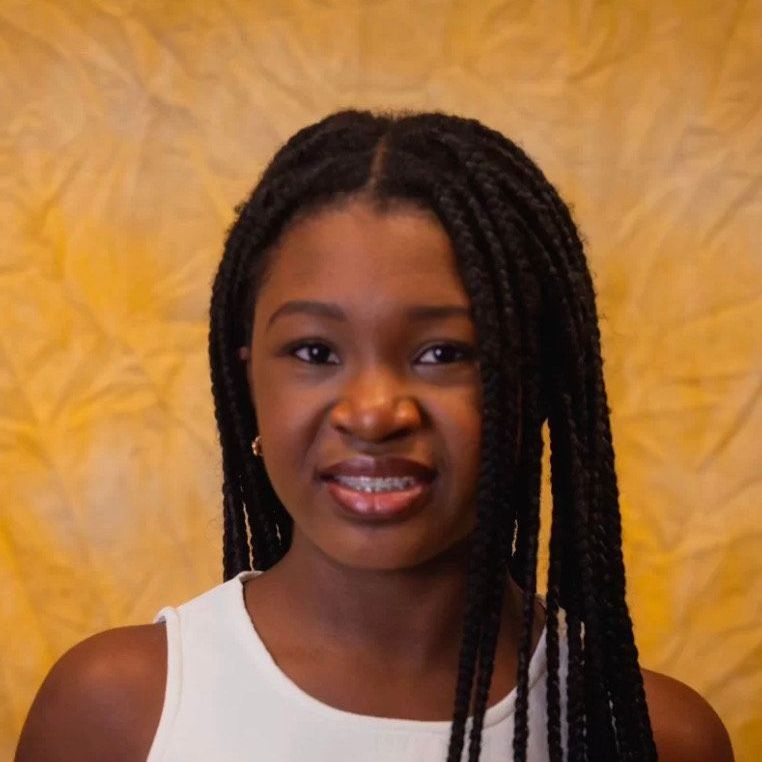 A woman with braids is smiling and wearing a white tank top