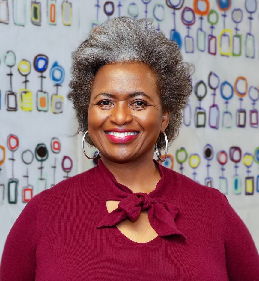 A woman with gray hair is smiling in front of a wall of women 's symbols