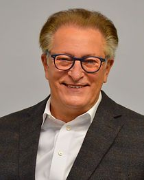 A man wearing glasses and a suit is smiling for the camera.