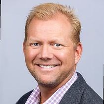 A man in a suit and plaid shirt is smiling for the camera.